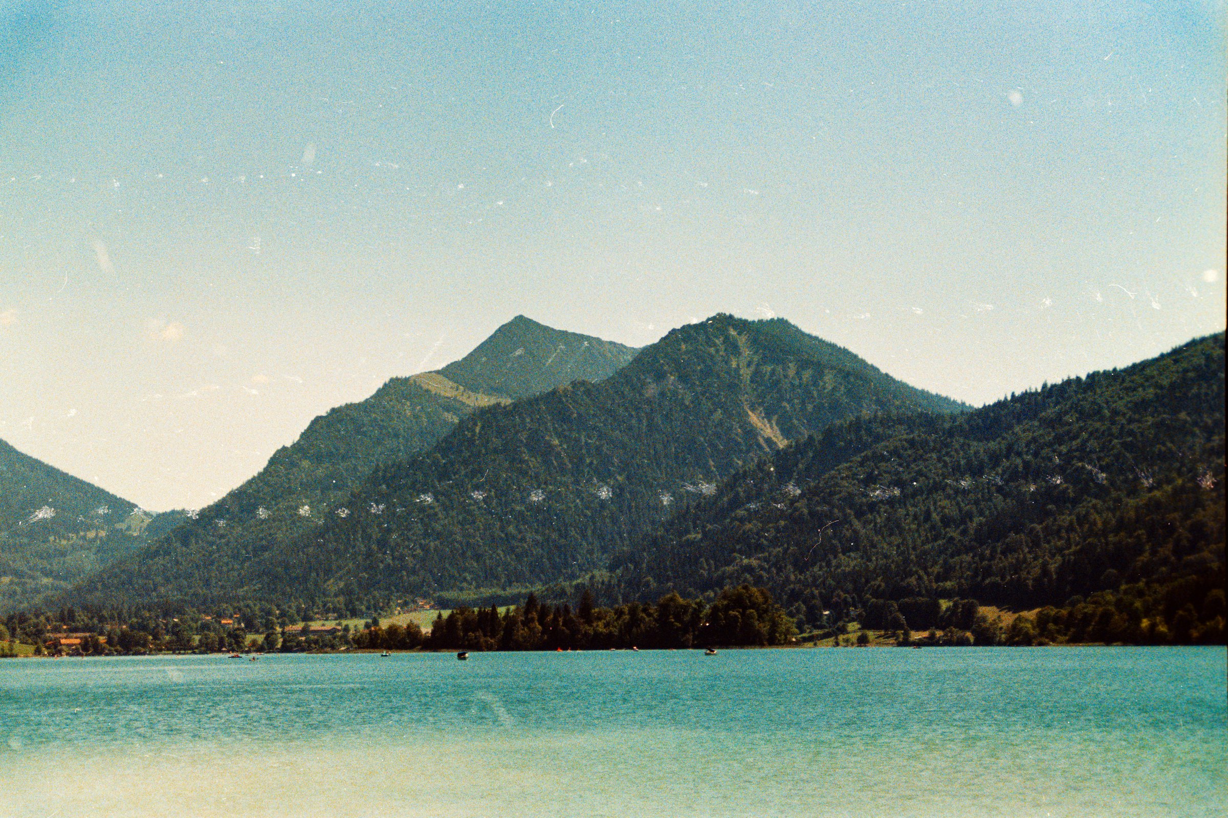 A turquoise lake below forested mountains under a clear sky